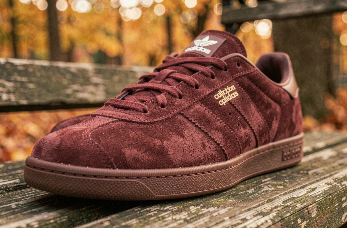 Gros plan des détails suède marron des sneakers Adidas Spezial posées sur un banc en bois en automne